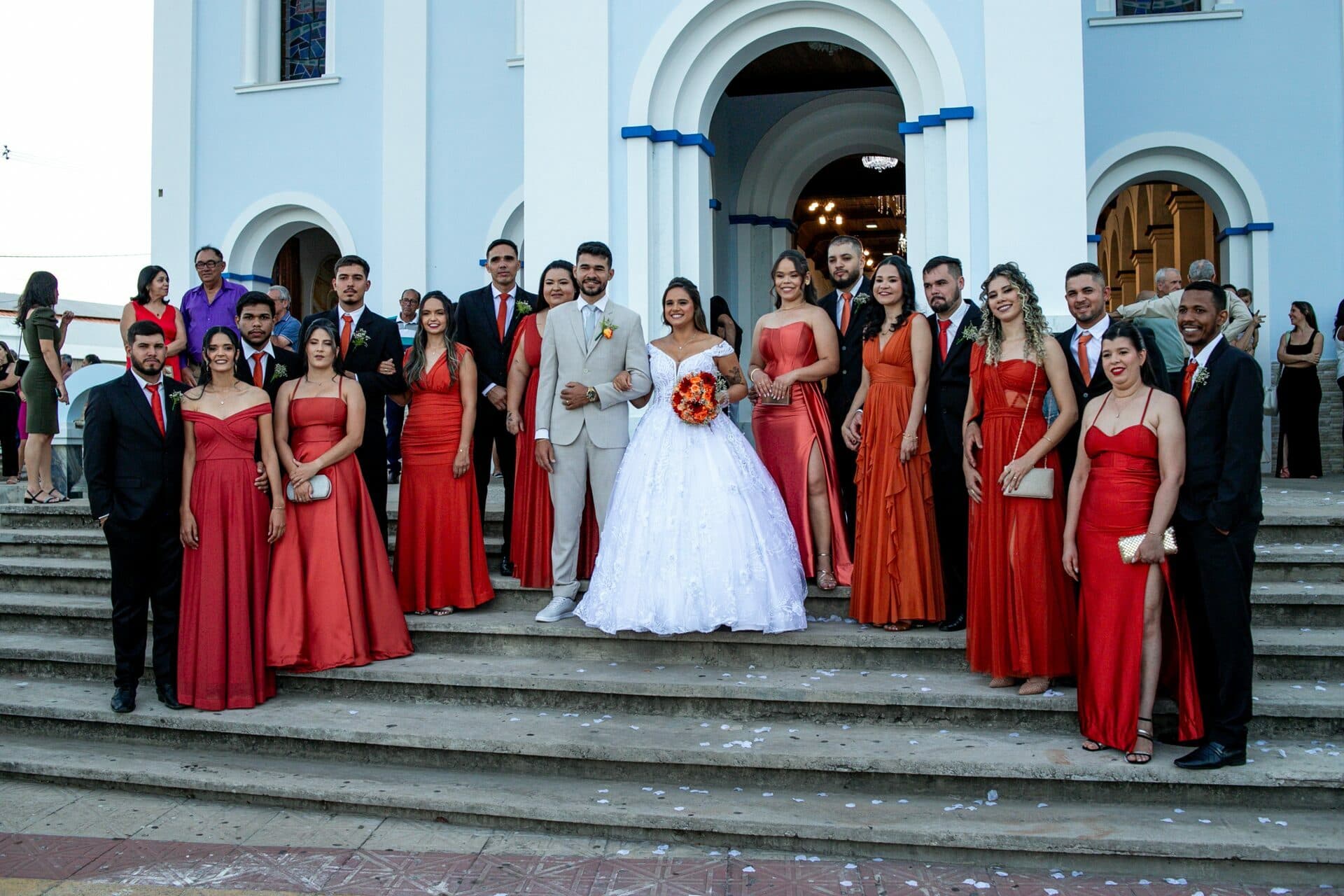 Casal com convidados nos degraus em frente à igreja.